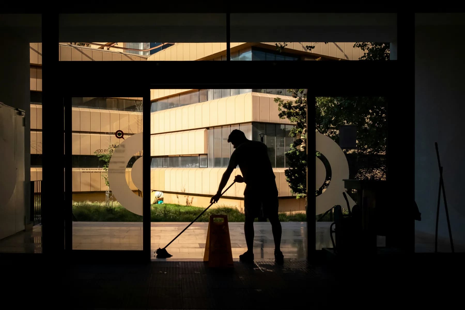 A cleaner mopping the floor inside a glass building entrance in the evening, an example of commercial cleaning on the gulf coast