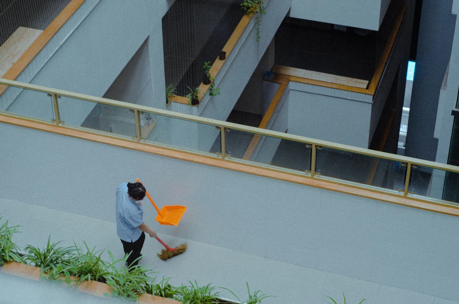 Overhead view of a worker sweeping an exterior walkway on a building balcony, an example of cleaning for gulf coast business districts