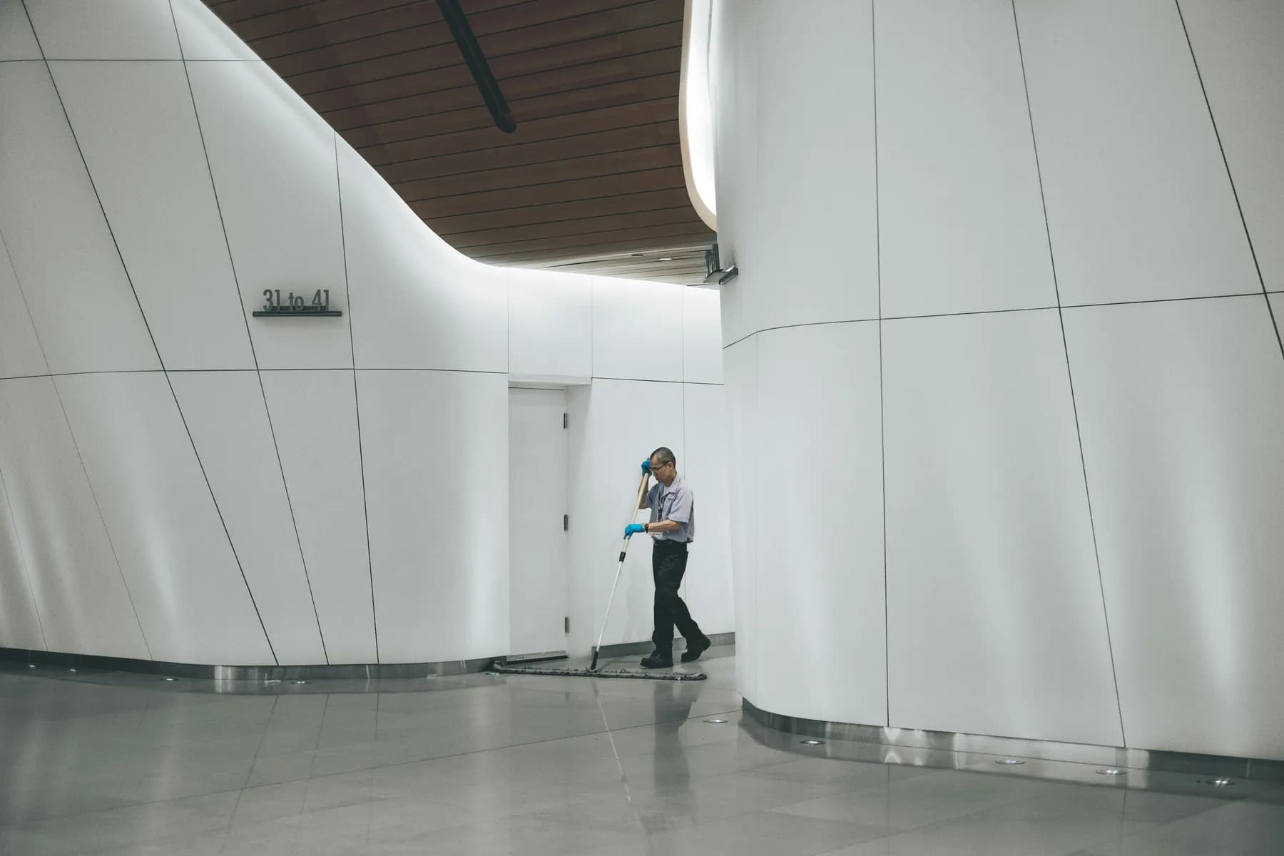 A cleaner flat-mopping a polished floor in a bright white building corridor