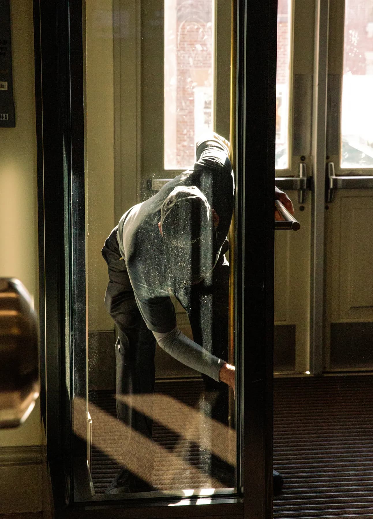 A worker cleaning the glass of a building entrance door in low evening light, an example of commercial cleaning on the gulf coast