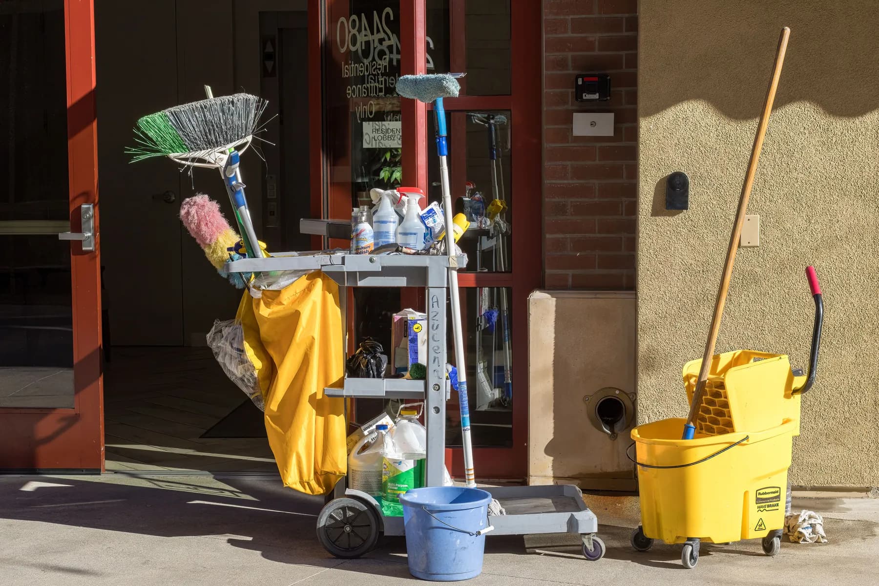 A janitorial cart, mop bucket and broom outside a residential building entrance, an example of school & daycare cleaning