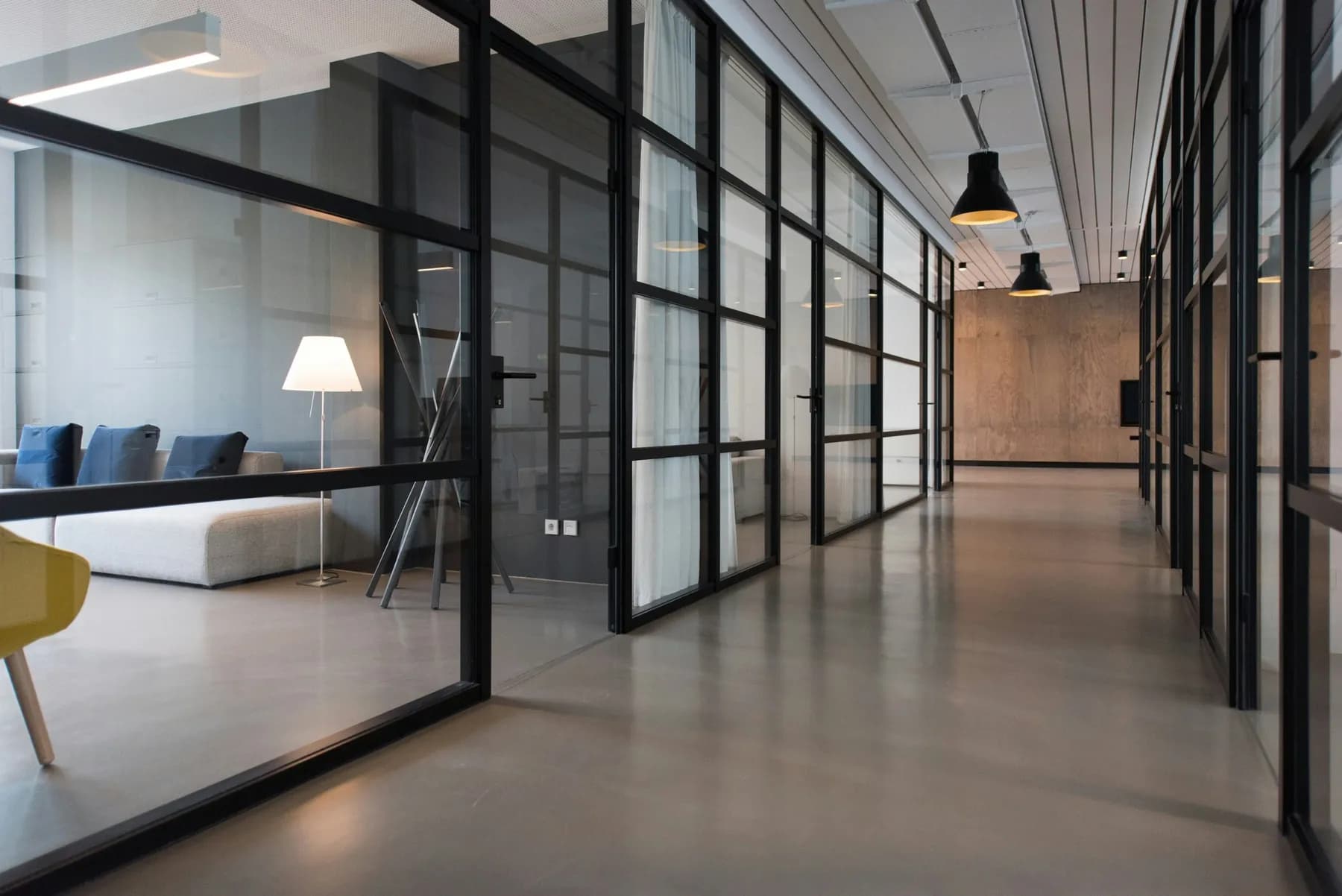 A clean, empty office corridor lined with glass-walled meeting rooms